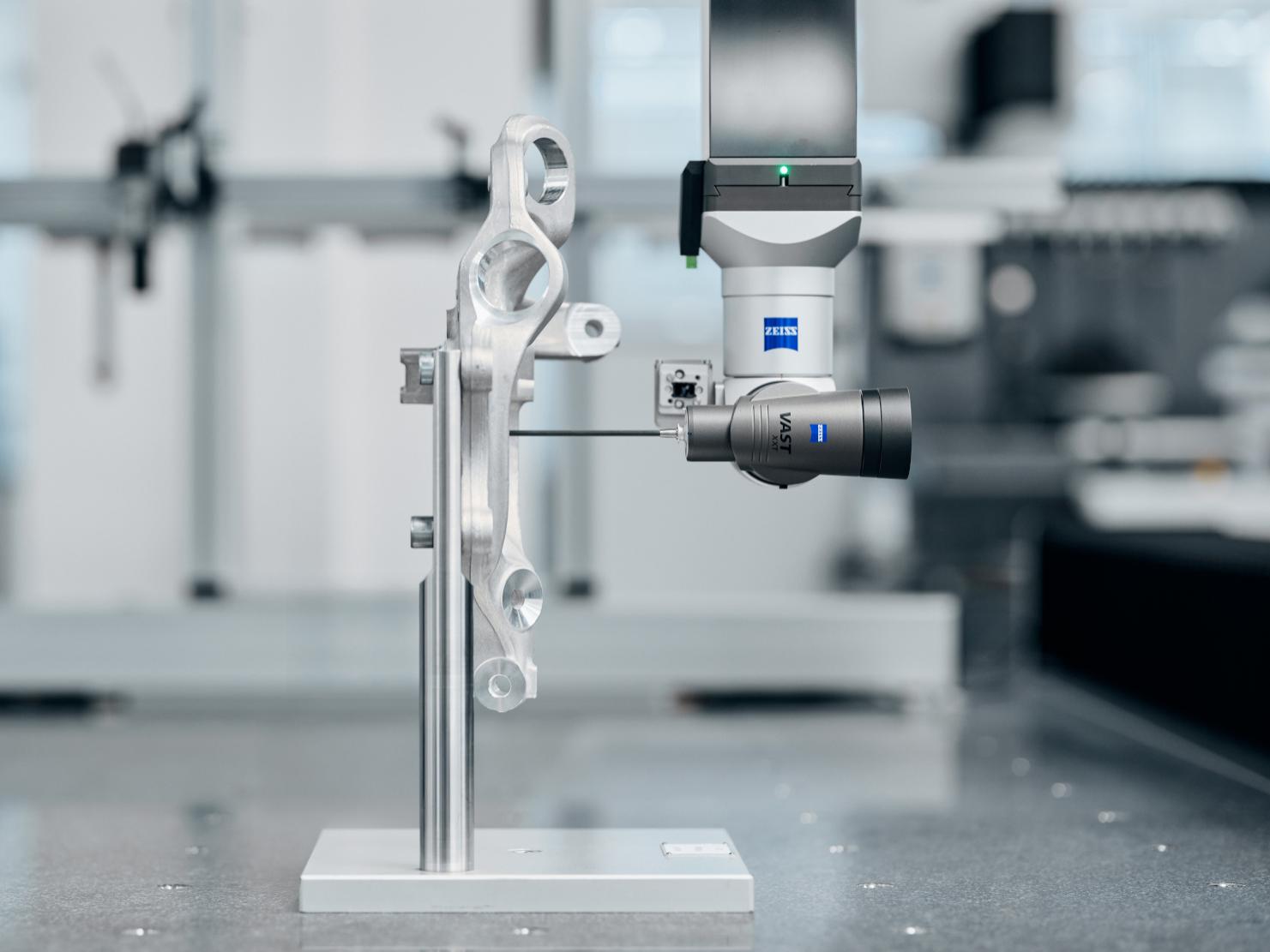 A ZEISS coordinate measuring machine VAST XXT compact design inspects a complex metal component in a high-precision laboratory setting.