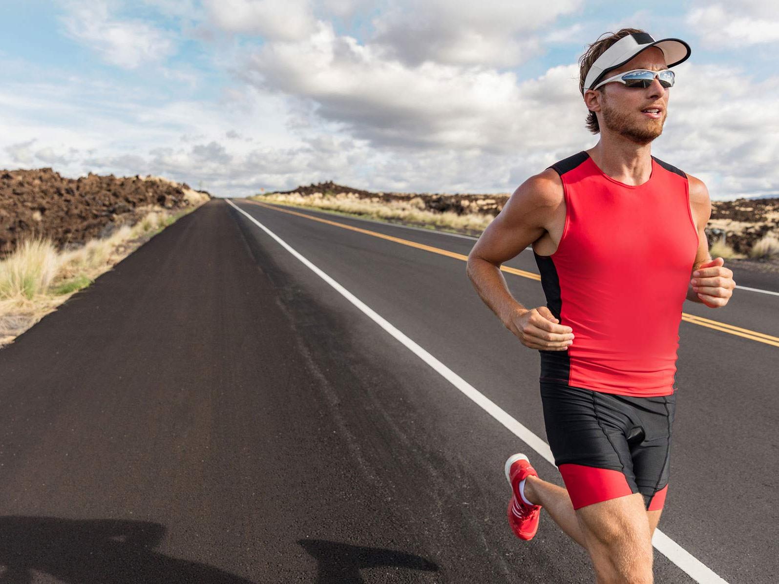 An image of a man wearing sports wear and sport lenses while running down a road. 