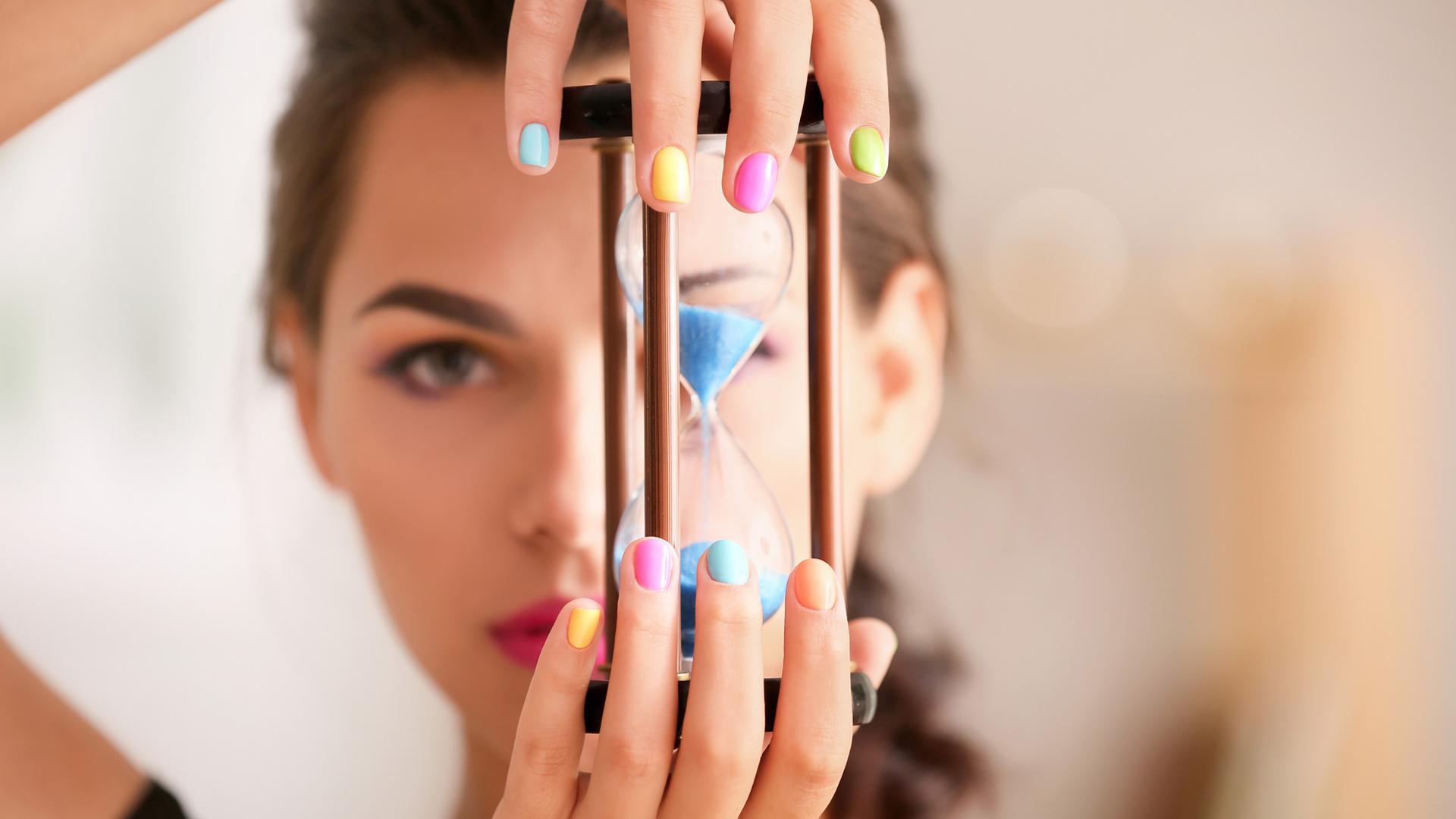 Young woman with colorful manicure holding hourglass