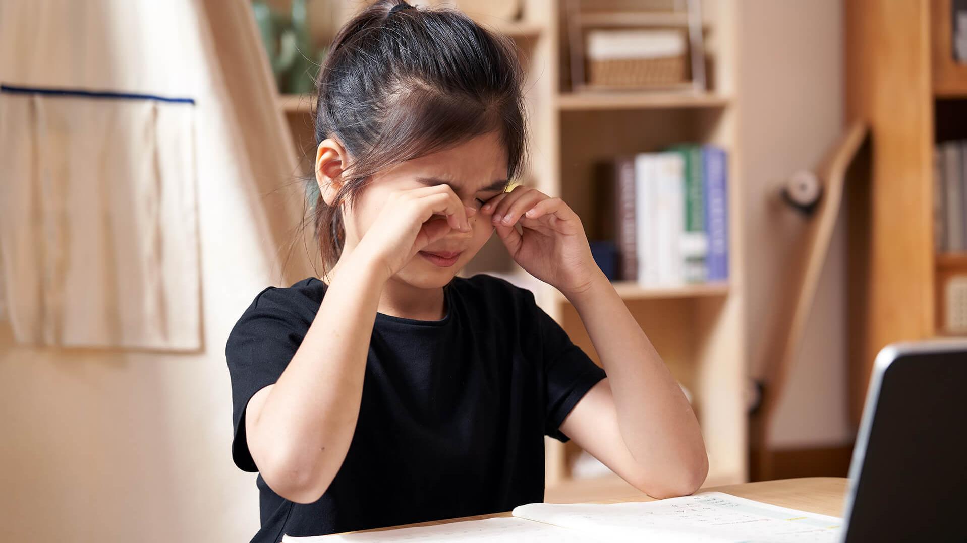 A little girl rubbing her eyes while doing school work.