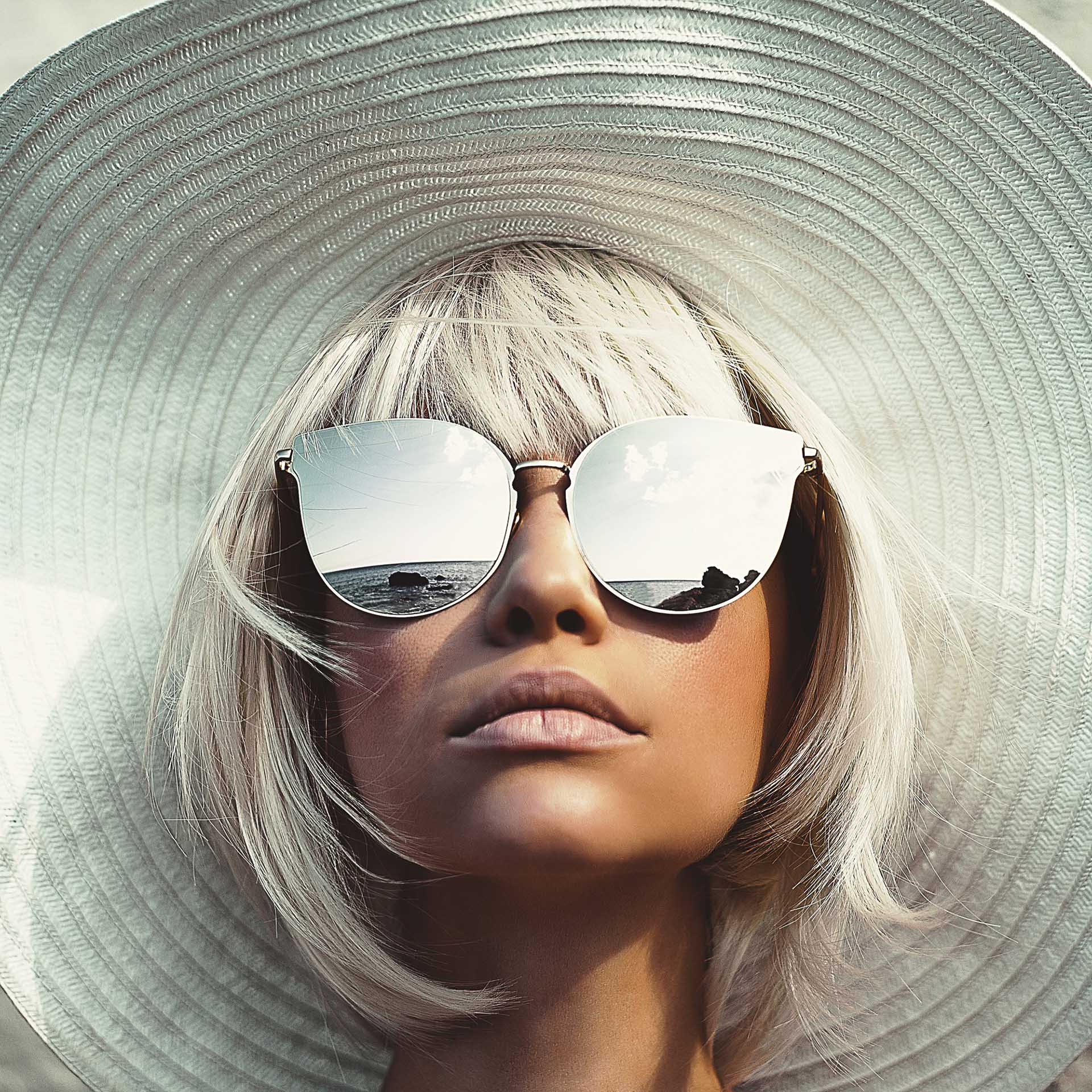  Young woman with big sun hat looks up and wears big sunglasses with mirror effect​.