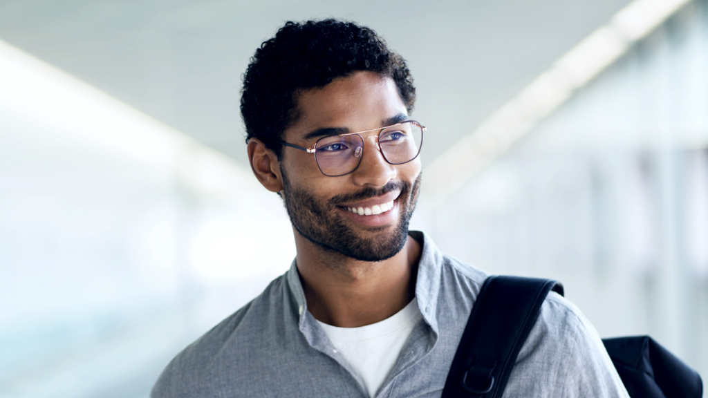 A young man smiling with a backpack over his shoulder is wearing ZEISS Digital SmartLife glasses and looking to the side.